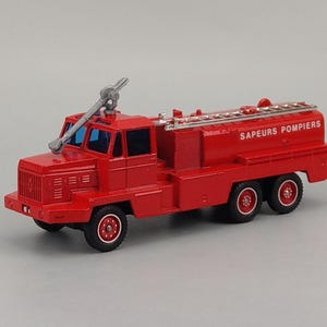 May include: A red toy fire truck with the words "Sapeurs Pompiers" printed on the side. The truck has a ladder on top and a silver nozzle. The wheels are black with red centers.