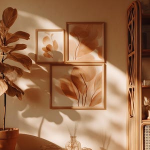 May include: A warm-toned interior scene featuring a potted plant with large, light brown leaves, and three framed botanical prints. A wooden bookshelf and a window with sunlight complete the cozy aesthetic. The artwork and plant create a natural, earthy vibe.
