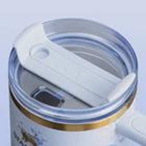 May include: Close-up of a white travel mug with a clear plastic lid. The lid has a sliding mechanism to open and close the drinking spout. The mug has a gold band and a floral design.