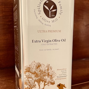 Może przedstawiać: Wysoka, prostokątna puszka z oliwą z oliwek z kremowym tłem i złotymi napisami i ilustracjami. Etykieta głosi "Extra Virgin Olive Oil" i "5000ml e". Marka to "Spiliotopoulos Family Olive Mill".