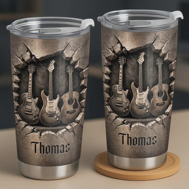 May include: Two stainless steel travel mugs with a guitar theme. Each mug features a design of guitars emerging from a stone wall, with the name "Thomas" printed at the bottom. The mugs have silver bases and lids.