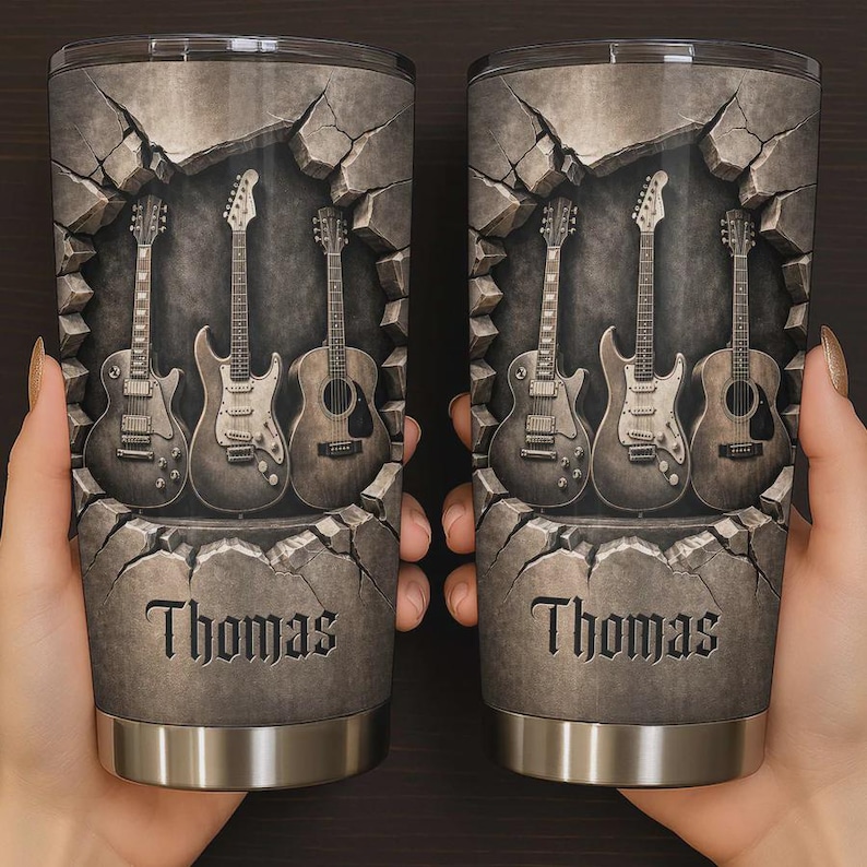 May include: Two stainless steel tumblers with a gray stone design featuring four guitars. The word "Thomas" is printed in a serif font on the front of each tumbler. The guitars are in a gray scale color.