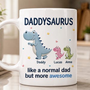 May include: White ceramic mug with the text "DADDYSAURUS" and three cartoon dinosaurs. The dinosaurs are blue, pink, and green, with the names "Daddy", "Lucas", and "Anna" below them. The mug also has the text "like a normal dad but more awesome".