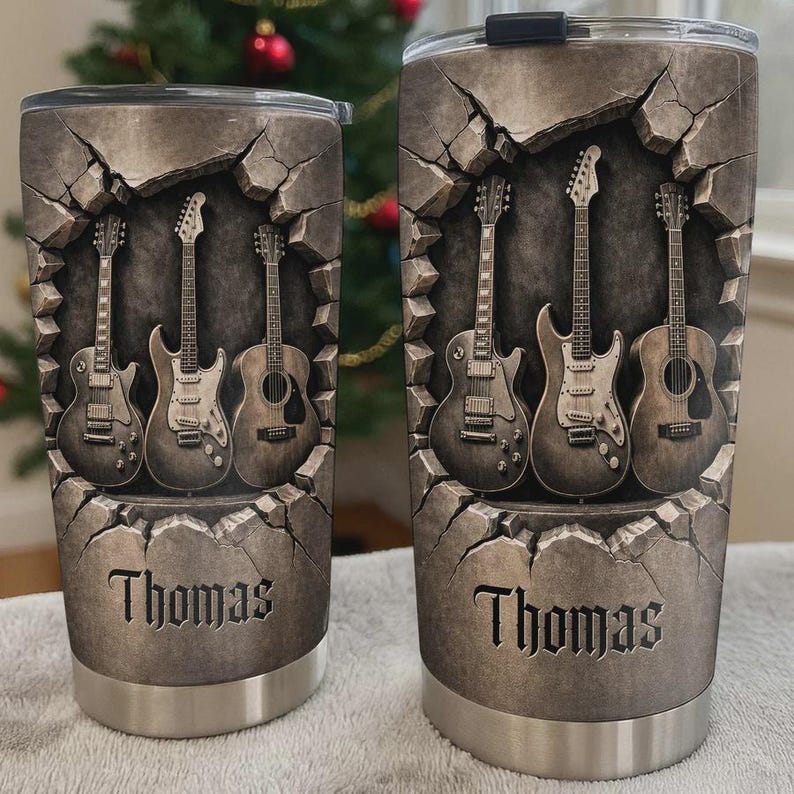 May include: Two stainless steel travel mugs with a rock-themed design. The design features four guitars emerging from a cracked stone wall, with the name "Thomas" at the bottom. The mugs have a silver base and black lids.
