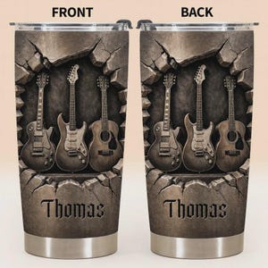 May include: Stainless steel tumbler featuring a design of three guitars emerging from a cracked stone wall. The name "Thomas" is displayed in a carved font at the bottom. The design is in shades of brown and gray.