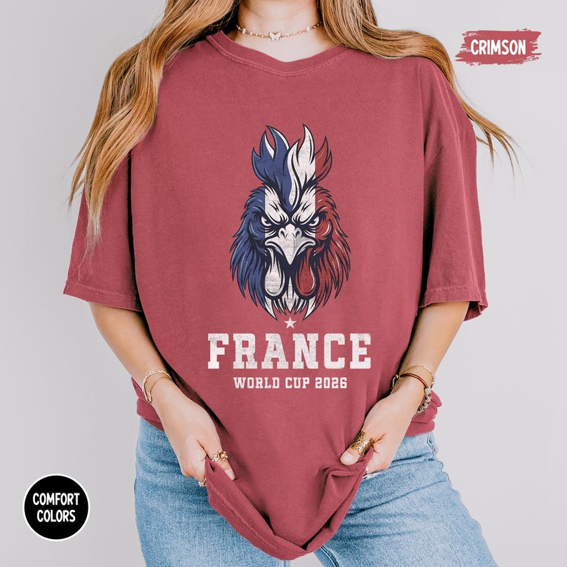 May include: Crimson-colored t-shirt featuring a detailed graphic of a rooster in the colors of the French flag. The word "FRANCE" is printed below the rooster, along with "WORLD CUP 2026". The shirt is a comfort color.