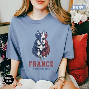 May include: A blue jean colored t-shirt featuring a rooster design in red, white, and blue, with the word "FRANCE" and "WORLD CUP 2026" printed below. The shirt is a comfort color.