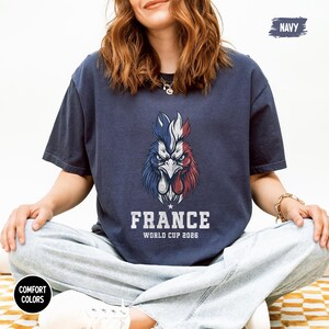 May include: Navy blue t-shirt featuring a stylized rooster in the colors of the French flag. The text "FRANCE WORLD CUP 2026" is printed below the rooster. The shirt is a comfort colors style.