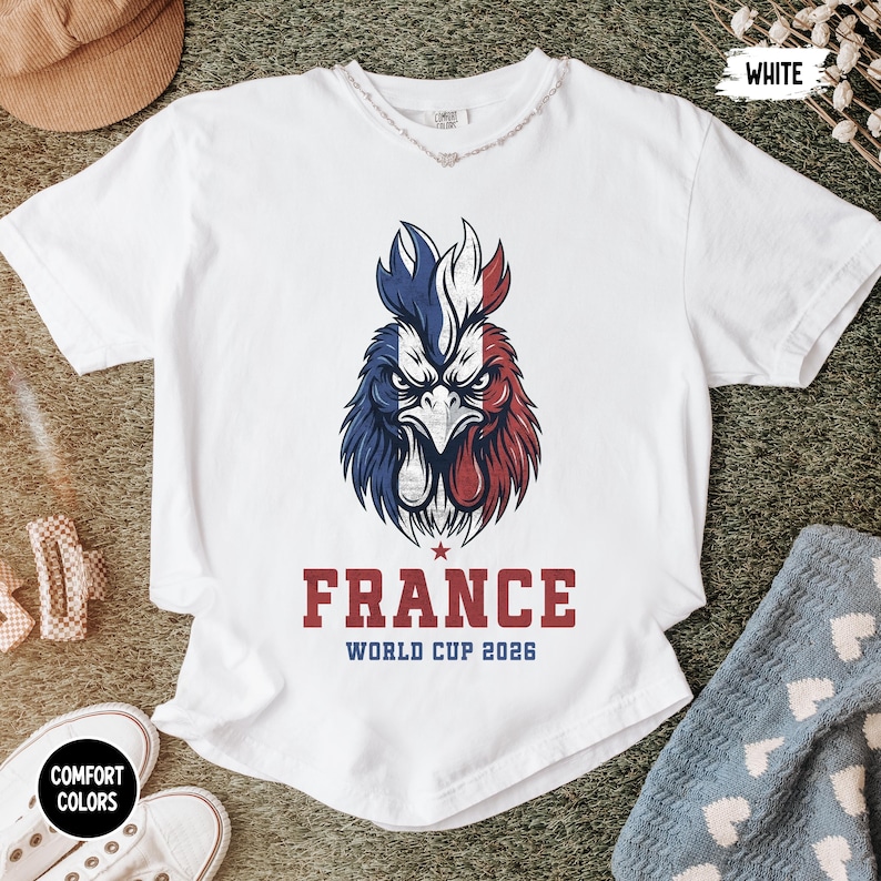 May include: White t-shirt featuring a rooster design in the colors of the French flag. The word "FRANCE" is printed in red, with "WORLD CUP 2026" below. The shirt is a Comfort Colors brand.