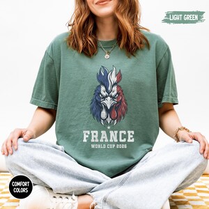 May include: Light green t-shirt featuring a rooster design in the colors of the French flag. The text "FRANCE WORLD CUP 2026" is printed below the rooster. The shirt is part of the Comfort Colors collection.