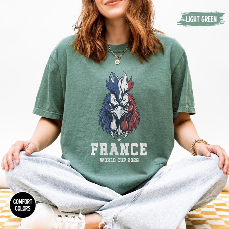 May include: Light green t-shirt featuring a rooster design in the colors of the French flag. The text "FRANCE WORLD CUP 2026" is printed below the rooster. The shirt is part of the Comfort Colors collection.