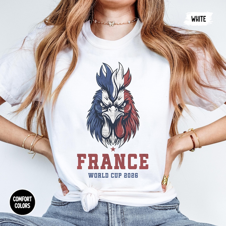 May include: White t-shirt featuring a detailed graphic of a rooster in the colors of the French flag. The word "FRANCE" is printed in a bold, red font, with "WORLD CUP 2026" below. The shirt also has "COMFORT COLORS" and "WHITE" printed on it.