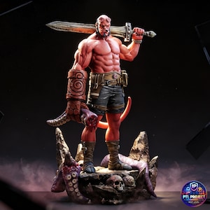 Op de afbeelding: Gedetailleerd beeldje van Hellboy, een roodhuidige demon, die een groot zwaard over zijn schouder houdt. Hij staat op een rotsachtige basis met schedels en tentakels. De figuur is gespierd en draagt een korte broek en laarzen.