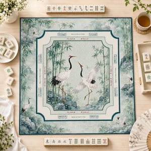 May include: A square Mahjong mat featuring a light green bamboo forest scene with two large cranes in the center. The mat includes printed game instructions and directional text like Charleston 1 and 2, Play Right, and Walls Left in English.