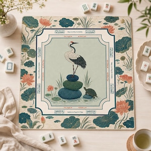 May include: A square Mahjong mat featuring a central illustration of a crane standing on stacked stones next to a turtle. The border displays lotus flowers and leaves on a cream background. Text includes Charleston instructions and directional arrows.