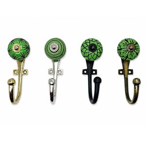 May include: Four wall hooks featuring round ceramic knobs in shades of green with black or gold decorative patterns. Each hook has a metal base in brass, silver, black, or antique bronze finish with two screw holes for mounting to a flat surface.