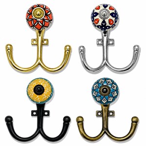 Peut inclure: Quatre patères doubles avec des boutons en céramique décoratifs. Le crochet en haut à gauche a une finition dorée avec un bouton rouge et blanc. Celui en haut à droite est argenté avec un bouton bleu et rouge. En bas à gauche, un crochet noir avec un bouton jaune et bleu, et en bas à droite, un crochet bronze avec un bouton bleu et blanc.
