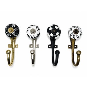 May include: Four wall hooks with round ceramic knobs featuring black and white patterns. The first has a gold finish, the second a silver finish, the third a matte black finish, and the fourth an antique brass finish, each with a mounting plate.