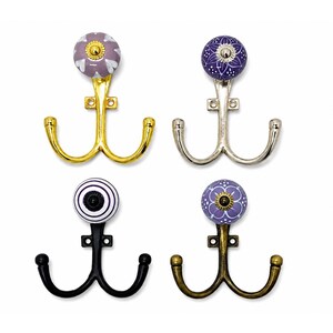 May include: Four double wall hooks with decorative ceramic knobs. The top left hook is gold with a lavender and white floral knob. The top right is silver with a purple and white floral knob. The bottom left is black with a striped knob. The bottom right is bronze with a purple and white floral knob.
