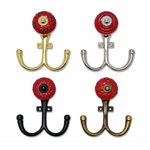 May include: Four double-pronged wall hooks featuring decorative circular knobs. The hooks come in gold, silver, black, and antique brass finishes. Each knob is red with intricate patterns and a central metallic accent, providing two hooks per unit.