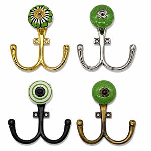 May include: Four double-pronged wall hooks featuring decorative ceramic knobs. The hooks come in gold, silver, black, and antique brass finishes. Each knob displays a unique green and white pattern, including floral, striped, and crackled designs.