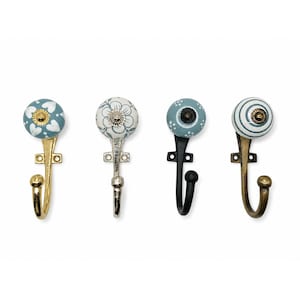 Puede incluir: Cuatro ganchos de pared con pomos de cerámica redondos y patrones variados que incluyen corazones blancos, motivos florales, puntos blancos y rayas azules. Cada gancho tiene una base de metal con placa de montaje y un brazo curvo con remate.