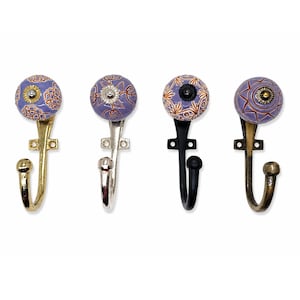 May include: Four wall hooks featuring round, lavender-coloured ceramic knobs with intricate orange floral and geometric patterns. Each hook has a distinct metal finish, including polished gold, silver, matte black, and antique brass tones.