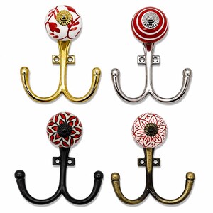 May include: Four double-pronged wall hooks featuring decorative ceramic knobs. The hooks come in gold, silver, black, and antique brass finishes. Each knob displays a unique red and white pattern, including floral, striped, and geometric designs.