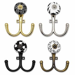 May include: Four double-pronged wall hooks featuring decorative ceramic knobs. The hooks come in gold, silver, black, and antique brass finishes. Each knob displays a unique black and white pattern, including floral, striped, and leaf motifs.