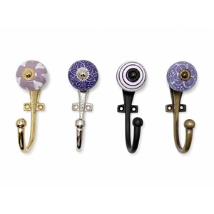 May include: Four wall hooks with round ceramic knobs. The first has a light purple floral pattern on a gold-tone metal hook. The second is dark purple with white floral details on a silver-tone hook. The third has purple stripes on a black hook.