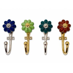 May include: Four wall hooks featuring flower-shaped heads in blue, light green, dark teal, and reddish-brown. Each hook has a metallic finish, a central circular detail on the flower, and a mounting plate with two screw holes for installation.