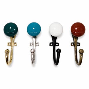 May include: Four wall hooks with round knobs, each featuring a different colour: dark green, bright blue, white, and reddish-brown. The hooks have metallic bases in gold, silver, black, and antique brass finishes, each with two screw holes.