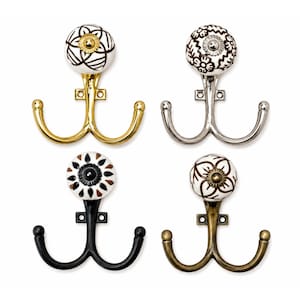 May include: Four double wall hooks with round ceramic knobs featuring various brown and black floral patterns. The hooks come in four distinct metal finishes: polished gold, polished silver, matte black, and an antique brass tone.