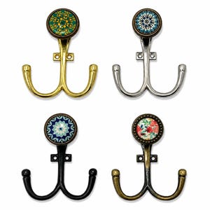 Può includere: Quattro ganci da parete doppi con estremità decorative circolari. I ganci presentano diverse finiture metalliche, tra cui oro, argento, nero e ottone anticato, ognuno sormontato da un inserto colorato con motivi floreali e geometrici.