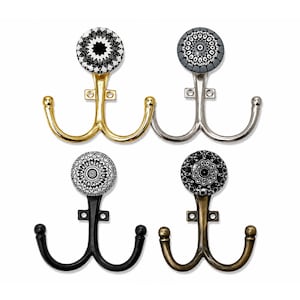 Può includere: Quattro ganci da parete doppi con pomelli decorativi circolari caratterizzati da intricati motivi geometrici bianchi e neri. I ganci presentano finiture in metallo oro lucido, argento, nero opaco e bronzo antico, ciascuno con piastra.