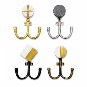 Könnte beinhalten: Vier Wandhaken mit zwei Zinken und dekorativen Oberteilen. Einer hat einen weißen Marmorkreis mit goldenem Kreuz, einer einen grauen, strukturierten Kreis mit silberner Basis, einer ein quadratisches weiß-goldenes Marmoroberteil und einer einen zweifarbigen Kreis.