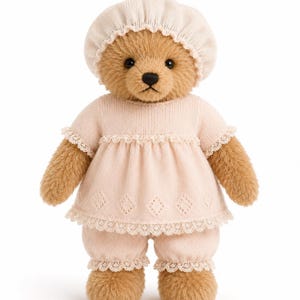 May include: A tan plush teddy bear wearing a light pink knitted outfit consisting of a short-sleeved top with lace trim and matching bloomers, paired with a coordinating light pink knitted bonnet that sits atop its round head.