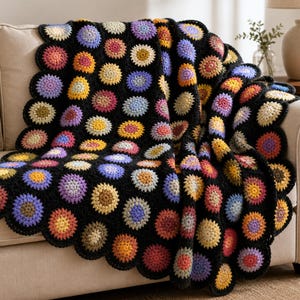Puede incluir: Una manta de ganchillo con un patrón repetitivo de motivos circulares en tonos amarillo, naranja, rosa, morado y azul, unidos por un fondo de lana negra con un borde festoneado que sigue la forma de los círculos individuales.