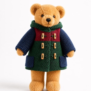 Könnte beinhalten: Ein Plüschteddybär mit hellbraunem Fell trägt einen gestrickten Dufflecoat mit Kapuze. Der Mantel hat einen dunkelroten Brustbereich, einen dunkelgrünen Körper und marineblaue Ärmel mit passenden Taschen. Er wird mit drei hellen Holzknebeln geschlossen.