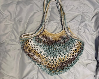 May include: A handmade crochet tote bag in a mix of colors including brown, white, teal, and gold. The bag features a textured, open weave design and a sturdy handle for carrying. The bag is designed to be a reusable shopping bag.
