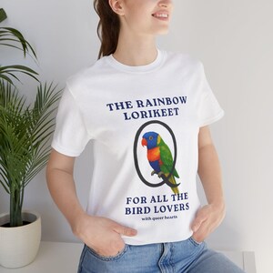 Op de afbeelding: Wit T-shirt met de tekst "THE RAINBOW LORIKEET" boven een kleurrijke papegaai-illustratie in een zwarte cirkel. Onder de illustratie staat de tekst "FOR ALL THE BIRD LOVERS with queer hearts".