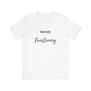 Puede incluir: Camiseta blanca con las palabras "Barely Functioning" impresas en negro. El texto está en una fuente sencilla y fácil de leer. La camiseta está hecha de un material suave y es adecuada para uso casual.