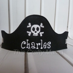 May include: Black felt pirate hat with a white skull and crossbones design and the name "Charles" embroidered in white.