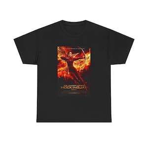 May include: Black t-shirt featuring a movie poster design. The poster depicts a figure with a bow and arrow against a fiery background. The text "The Hunger Games: Mockingjay - Part 2" is visible.