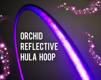 May include: A purple and white reflective hula hoop with the text "ORCHID REFLECTIVE HULA HOOP" on it. The hoop is surrounded by a trail of sparkling lights.