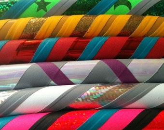 May include: A collection of colourful hula hoops with a spiral design. The hoops display a variety of colours, such as green, blue, red, yellow, and pink, with glitter, star, and moon details. The hoops are stacked together.
