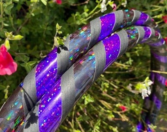May include: A black and purple hoop with iridescent glitter. The hoop is made of plastic and has a black tape wrap.