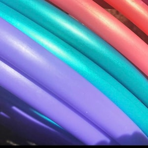 May include: Close-up of a set of colorful plastic hoops, with a teal, purple, and pink hoop stacked on top of each other.