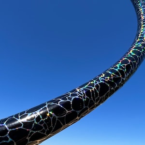 May include: Close-up of a black hoop with a silver and iridescent crackle finish. The hoop is curved and the background is a bright blue sky.