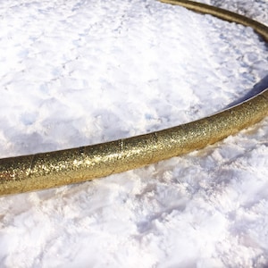 May include: A gold glitter hula hoop on a white fluffy surface.